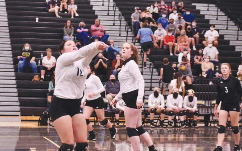 Claire Villadsen, foreground, sets the ball for Rylee Sherman, center.