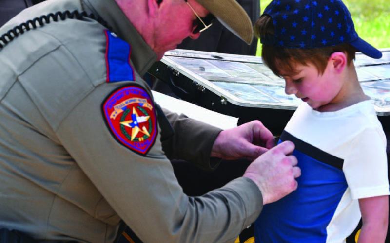DPS Trooper Alt affixes a sticker to a child’s shirt at the annual Cops N Kids picnic held Friday at Claiborne West Park. The event is sponsored by the Orange County Sheriffs’ Department.