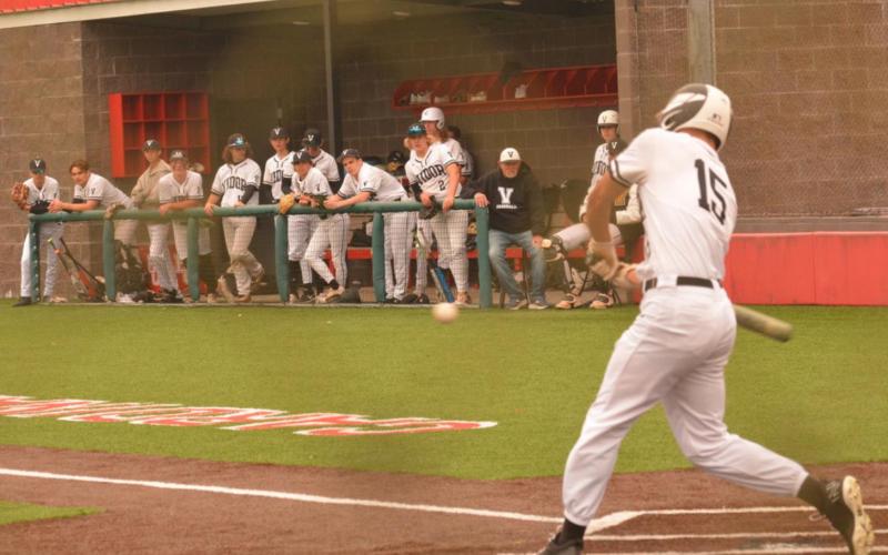 Jarrett Odom starts his swing as Pirate teammates look on from the dugout at the Bridge City baseball tournament. Photo by Randall Luker