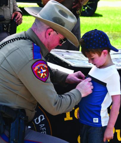 DPS Trooper Alt affixes a sticker to a child’s shirt at the annual Cops N Kids picnic held Friday at Claiborne West Park. The event is sponsored by the Orange County Sheriffs’ Department.
