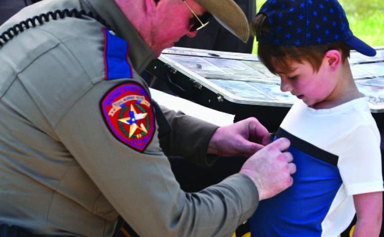 DPS Trooper Alt affixes a sticker to a child’s shirt at the annual Cops N Kids picnic held Friday at Claiborne West Park. The event is sponsored by the Orange County Sheriffs’ Department.